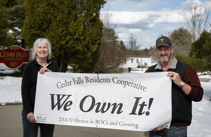 Two residents and members of the Cedar Falls Residents Cooperative holding a sign saying "We Own It!"