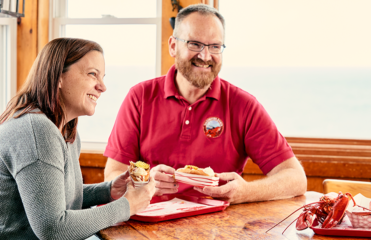 Restaurant owners sitting down at a table eating lobster rolls